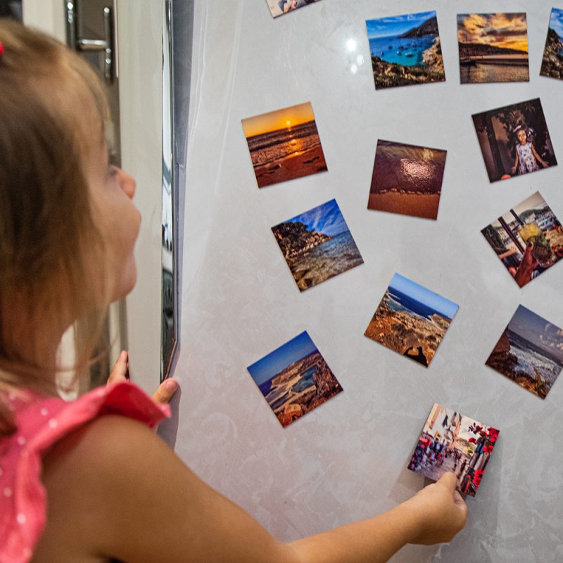 Bambina che attacca delle calamite fotografiche su un frigo con altri magneti fotografici